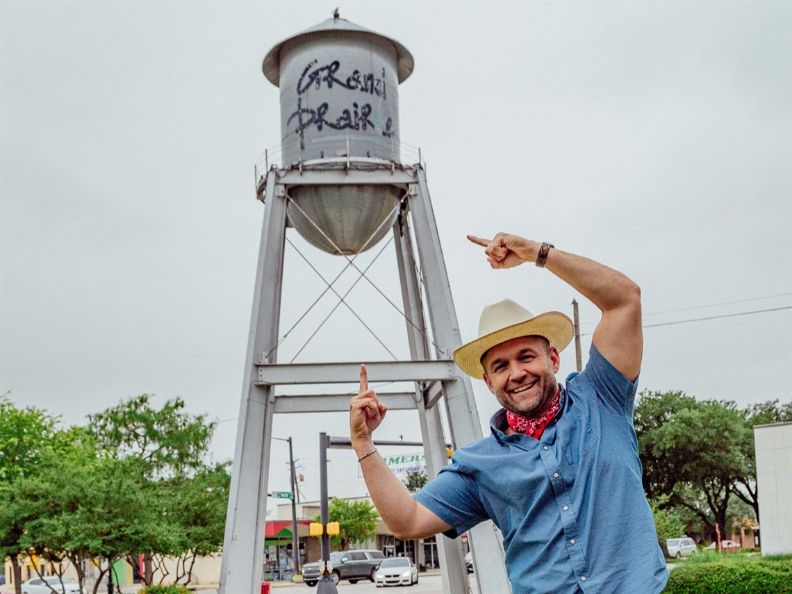 Man posing under Daytripper Water Tower in Grand Prairie, pointing upward
